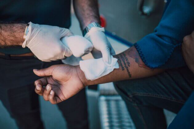 Gloved hands applying a bandage to a person’s wrist.