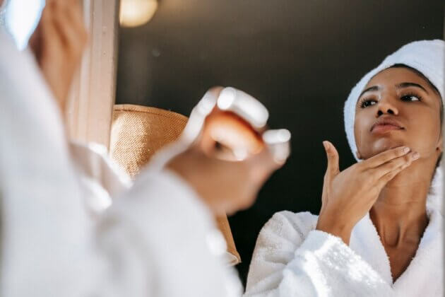Woman applying skincare cream while looking in a mirror.