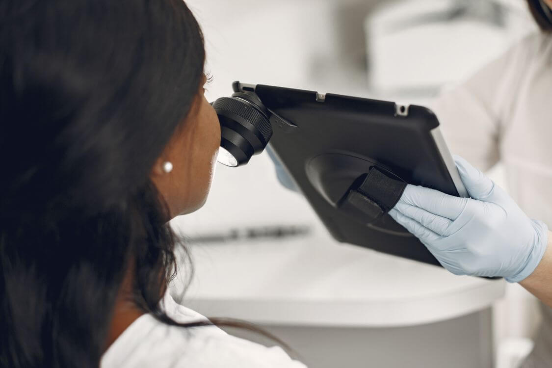 Clinician using a digital skin examination device with a tablet.